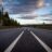 gray concrete road between green trees under gray clouds